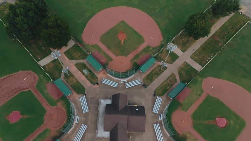 Aerial drone footage slowly descends over an empty, symmetrical five-diamond baseball and softball complex