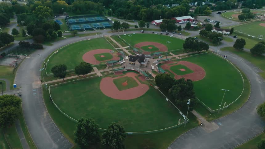 A slow, rising, and rotating aerial view of a unique four-leaf clover-shaped baseball field complex at a local park