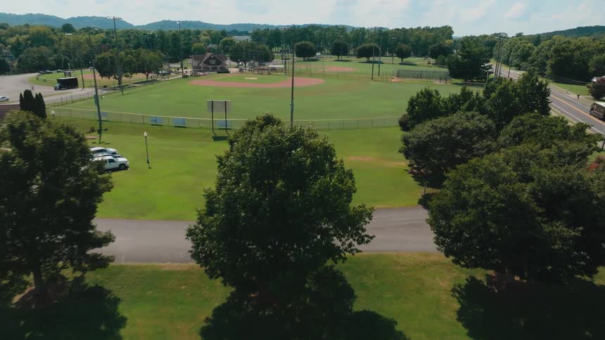 Aerial drone footage flying over a beautiful, empty baseball field complex on a sunny day