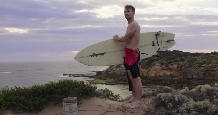 Man holding a surfboard looks out at the water