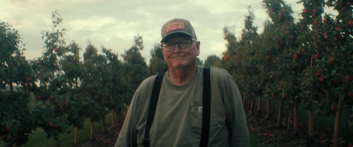 Portrait of a proud elderly farmer smiling warmly while standing in his apple orchard at dusk
