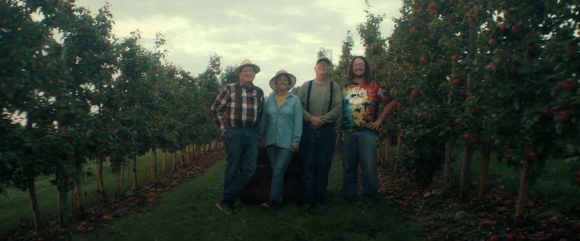 A proud group of four diverse farmers pose for a portrait in the middle of a beautiful apple orchard