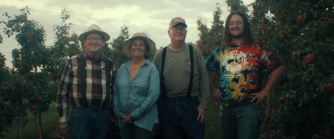 A family of apple farmers stand proudly together for a portrait amidst the rows of fruit-laden trees