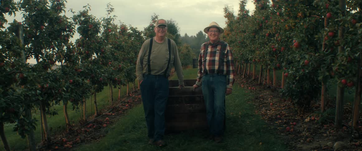 Two smiling elderly farmers stand for a portrait in their apple orchard