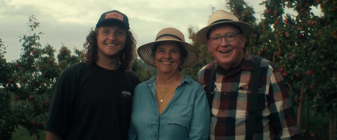 A happy family of three farmers poses for a portrait in their beautiful apple orchard
