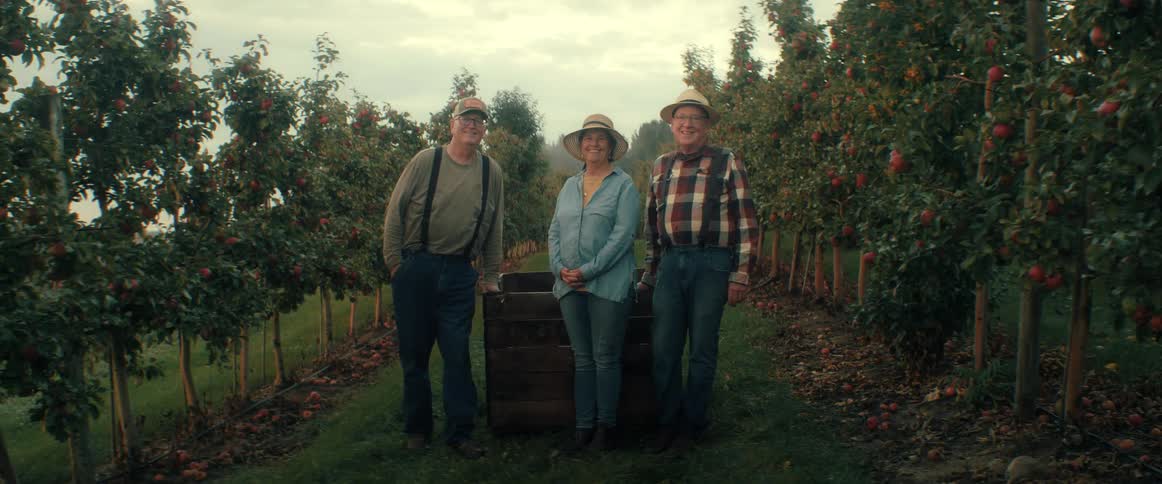 Three joyful senior farmers laugh and smile for a portrait in their apple orchard during the fall harvest