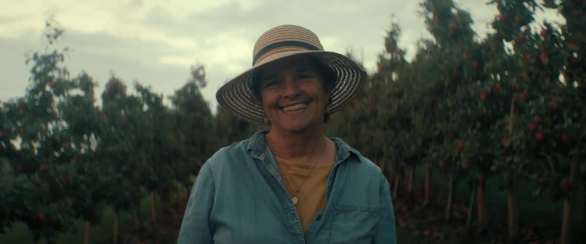 Happy senior female farmer in a straw hat smiles while standing in an apple orchard