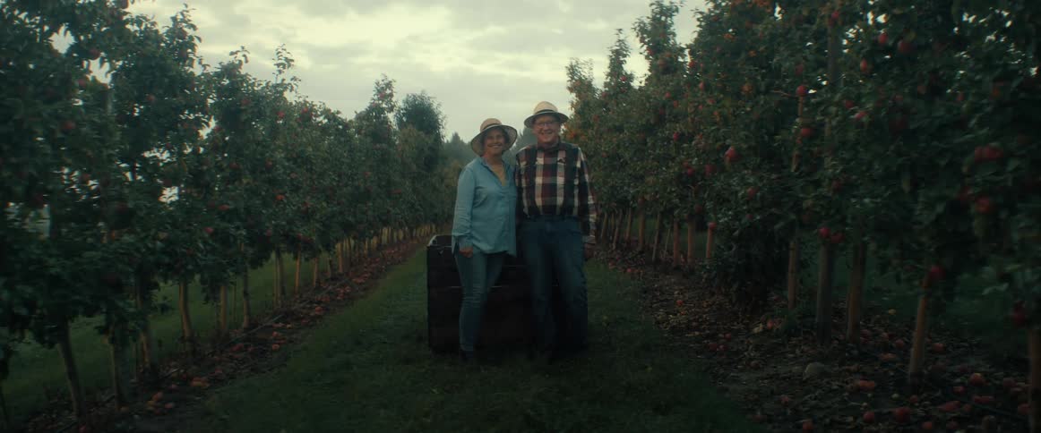 A happy senior farmer couple stands together for a portrait in the middle of their apple orchard