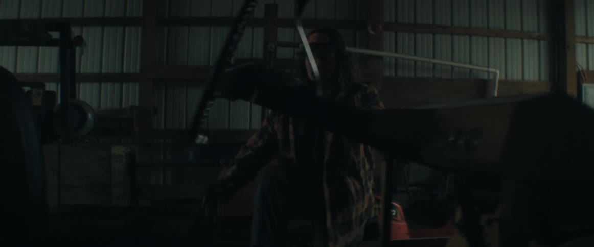 A young male farmer in a flannel shirt climbs aboard his vintage yellow tractor inside a dark, rustic barn to begin his day