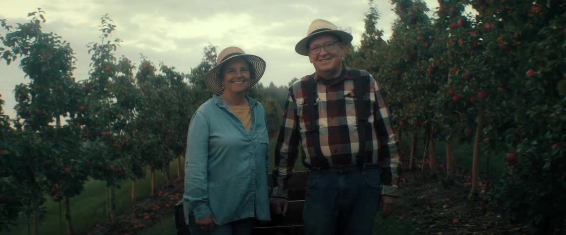 Happy senior farming couple smiles for a portrait in their beautiful apple orchard at dusk