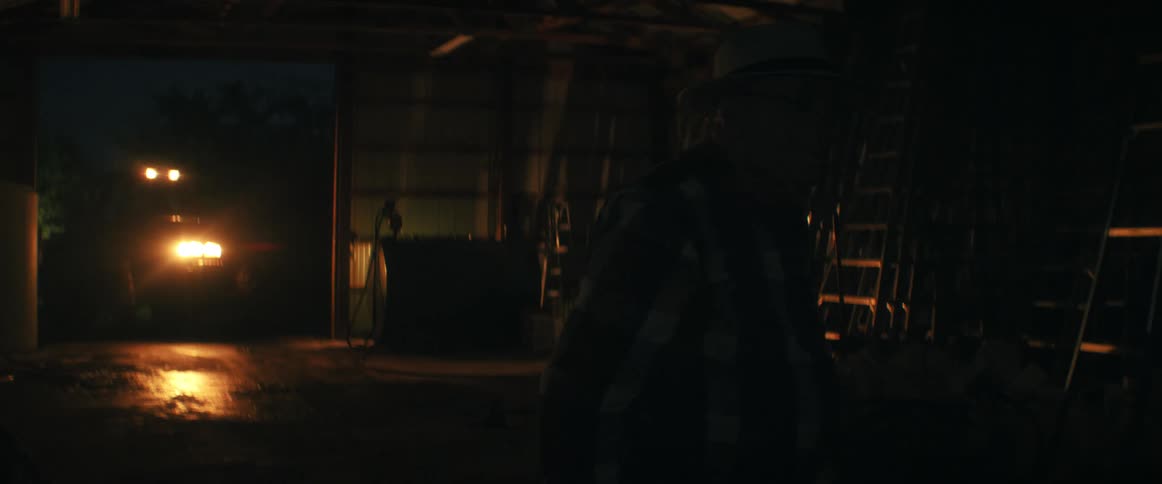 An elderly farmer in a dimly lit barn gets emotional, putting on his hat and walking away into the darkness