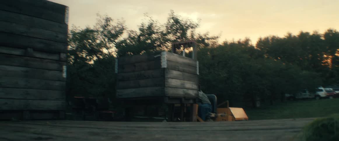 An orchard worker operates a forklift, transporting a large wooden crate filled with harvested apples onto a loading dock at sunset