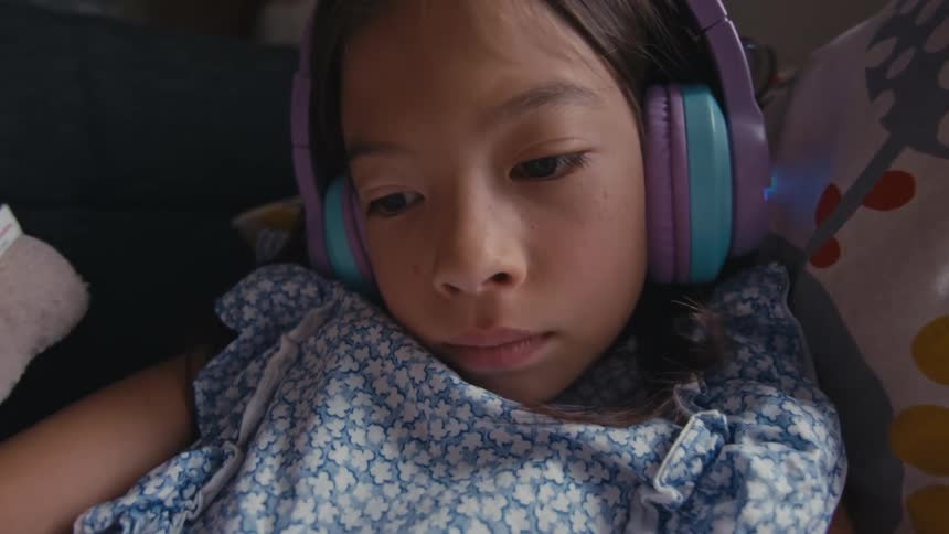 Close up of a little girl wearing light-up headphones while resting on a couch at home