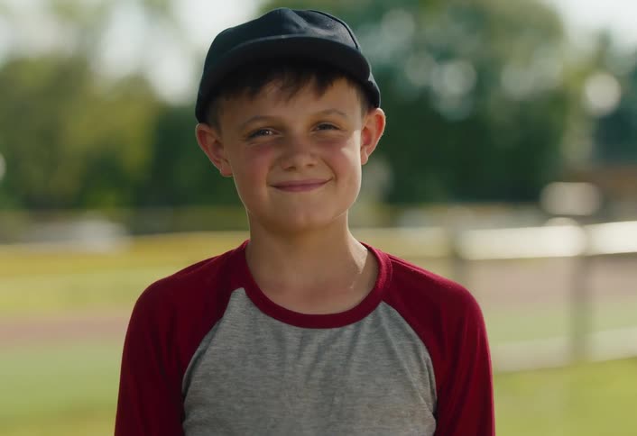 Portrait of a happy boy in a baseball cap smiling at the camera on a sunny day at the field