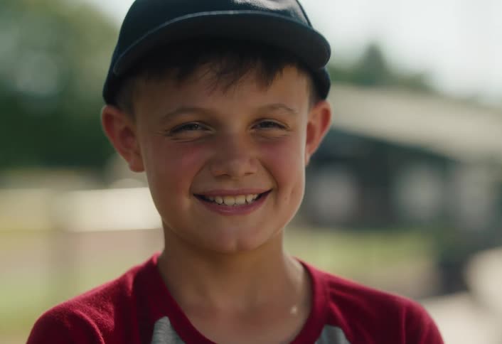 Close-up portrait of a happy young boy with a big smile, wearing a baseball cap outdoors