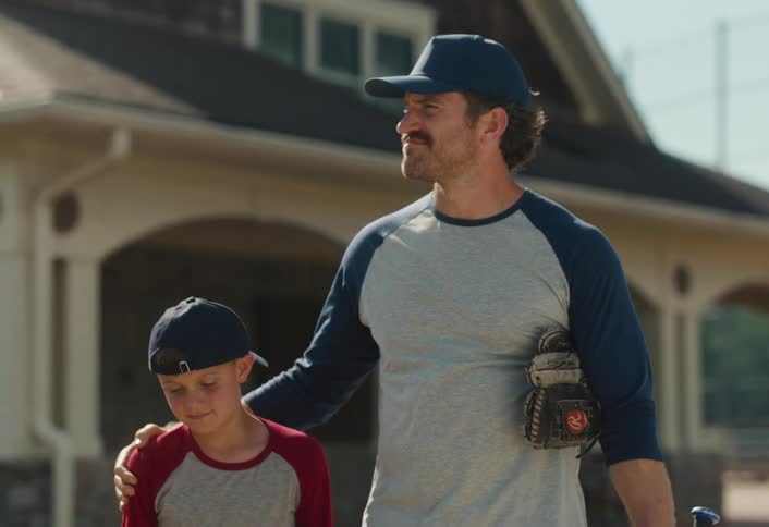 A caring father consoles his disappointed son with a supportive arm around his shoulder as they walk off the baseball field together after a game