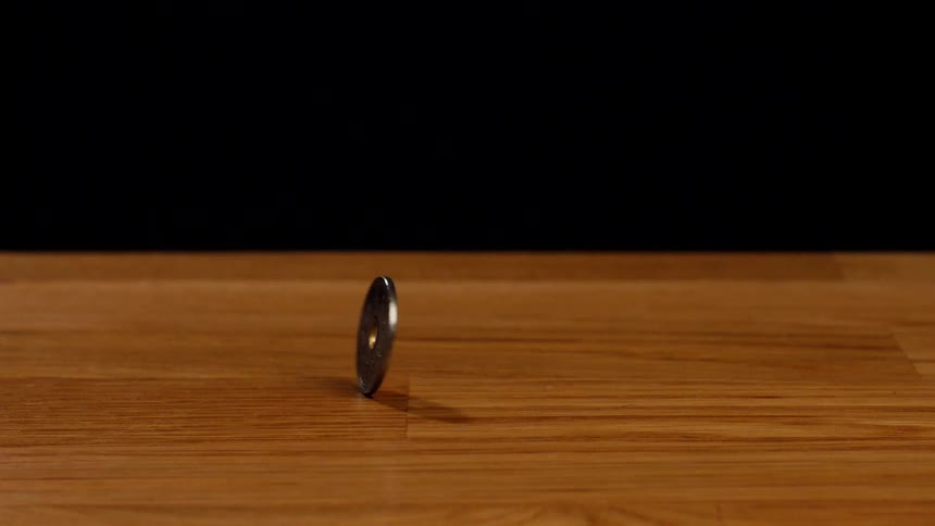 A Japanese 5 yen coin spins in a seamless loop on a wooden table against a black background