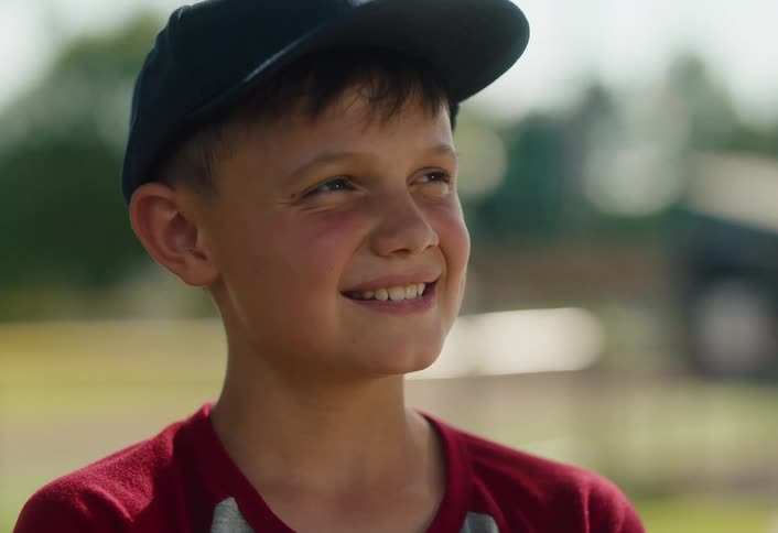 Portrait of a joyful young boy in a baseball cap smiling hopefully while outdoors on a sunny day