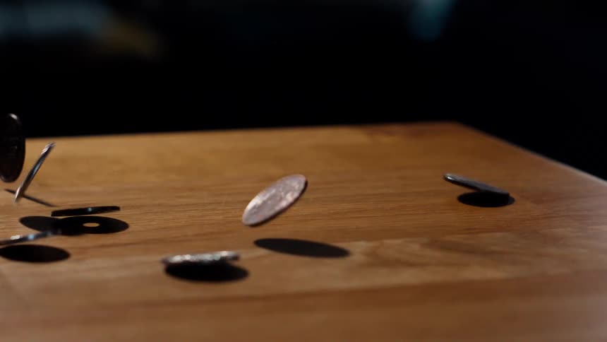 A shower of Japanese Yen coins tumbles and spins across a wooden tabletop in dramatic slow motion