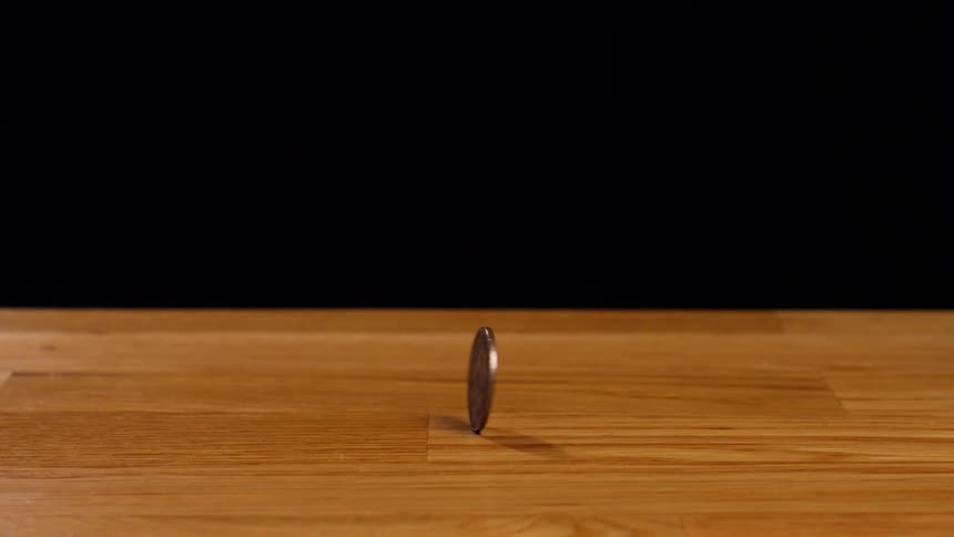 A 2 Euro coin spins in slow motion on a wooden table against a black background in a perfect loop
