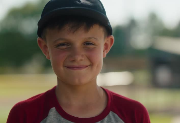 Slow motion portrait of a happy young boy in a baseball cap smiling at a baseball field