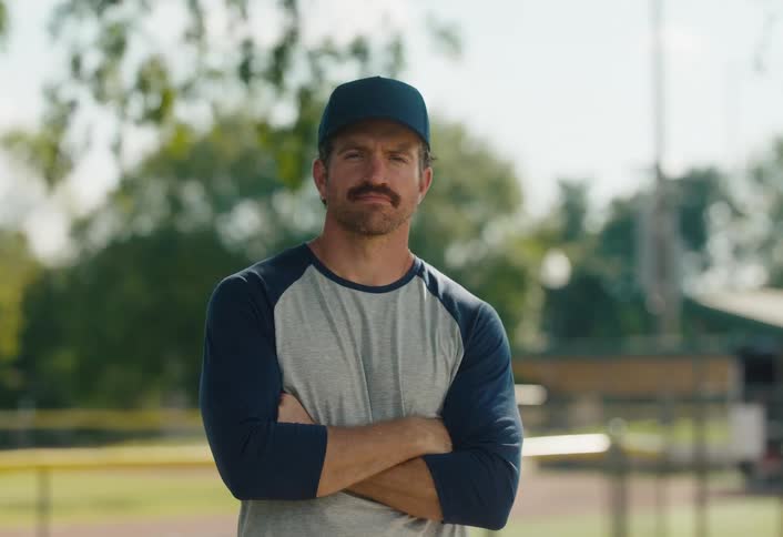 Portrait of a serious baseball coach with a mustache standing on a baseball field with his arms crossed