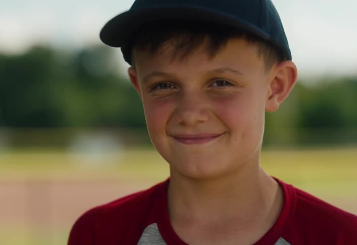 A close-up portrait of a happy young boy in a baseball hat smiling directly at the camera
