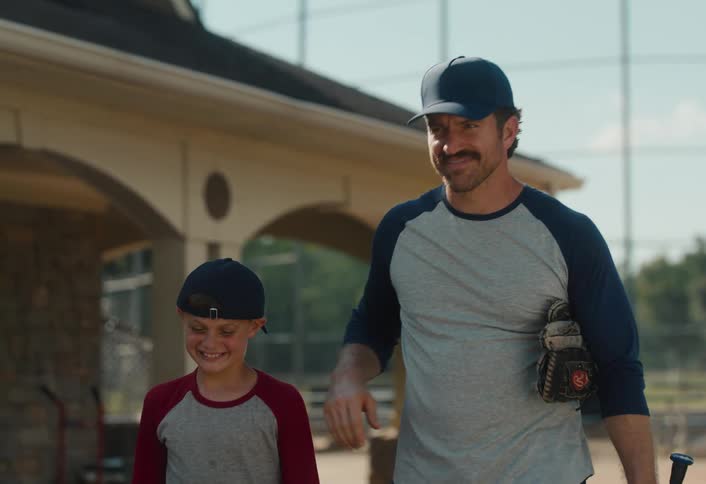 A proud father pats his smiling son on the head and shoulder as they walk together off a baseball field in slow motion