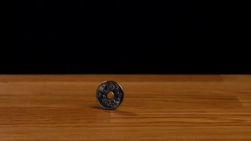 A Japanese 50 yen coin spins on a wooden surface against a stark black background
