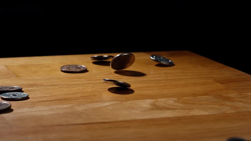 A variety of Japanese Yen coins fall in dramatic slow motion onto a wooden table against a black background