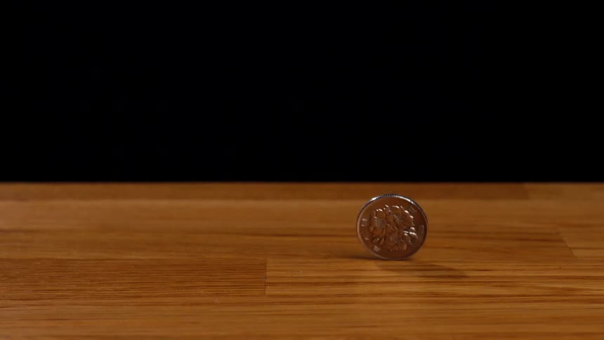 A Japanese 100 yen coin spins in mesmerizing slow motion on a wooden table before wobbling to a stop