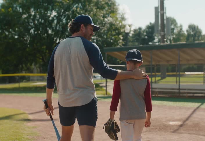 A supportive father walks with his arm around his son after a baseball game in slow motion