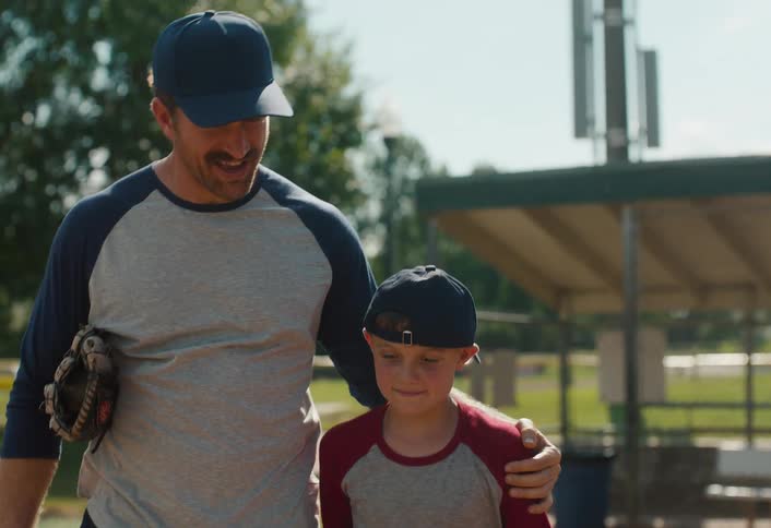 A proud father walks with his arm around his son, offering words of encouragement after a baseball game in slow motion