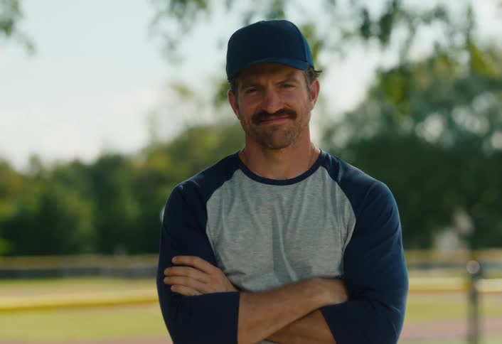 Portrait of a smiling and confident baseball coach with a mustache standing on a sunny field