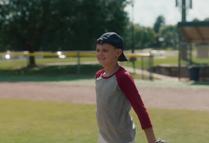 Slow motion shot of a happy young boy throwing and catching a baseball on a sunny day at the park