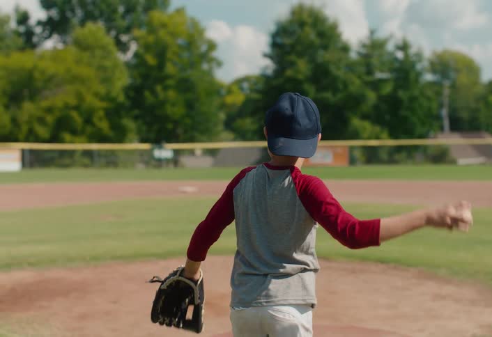 A young boy practices pitching and throwing with his father on a baseball diamond in slow motion