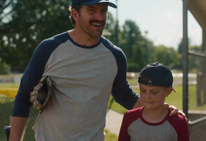 A father and his son walk together onto the baseball field, sharing a happy moment before practice in slow motion
