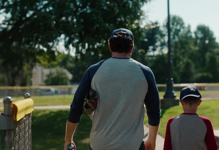 Rear view in slow motion of a proud father walking with his arm around his son after baseball practice at the park