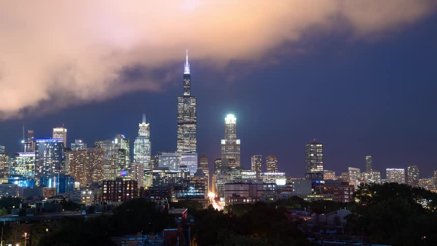A mesmerizing night time-lapse captures the illuminated Chicago skyline with clouds rolling over the iconic Willis Tower