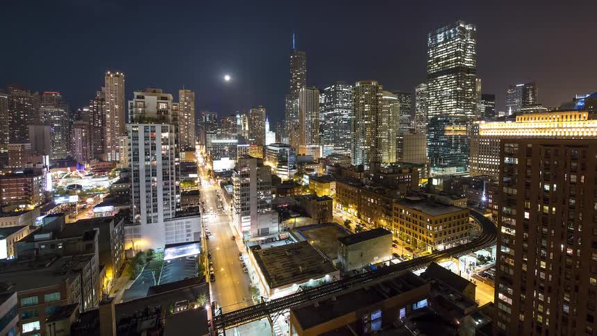 A captivating night time-lapse of the Chicago skyline with the full moon overhead and busy traffic and L trains moving through the city streets