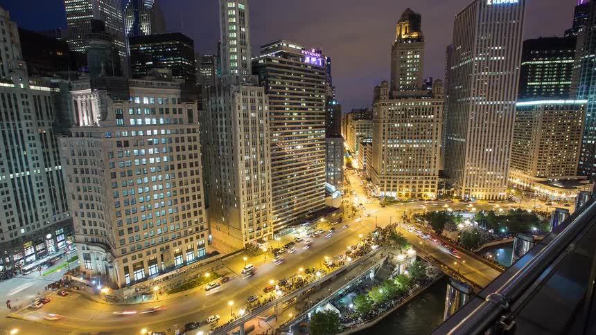 A high-angle time-lapse captures the vibrant energy of downtown Chicago at night, with traffic streaming over bridges and along the river