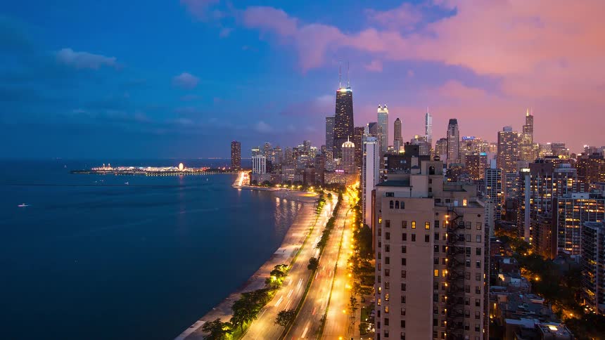 A vibrant timelapse of the Chicago skyline at dusk showing traffic light trails along Lake Shore Drive next to Lake Michigan