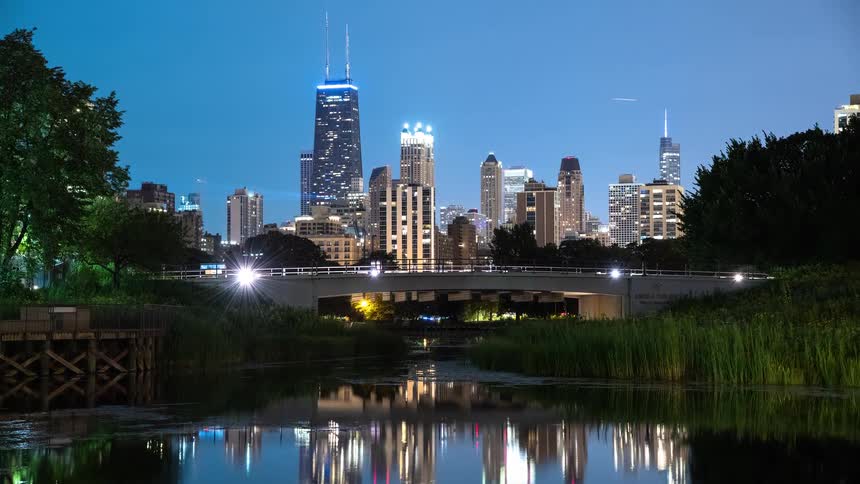 A serene night timelapse of the iconic Chicago skyline with its glittering skyscrapers perfectly reflected in the tranquil waters of Lincoln Park's South Pond