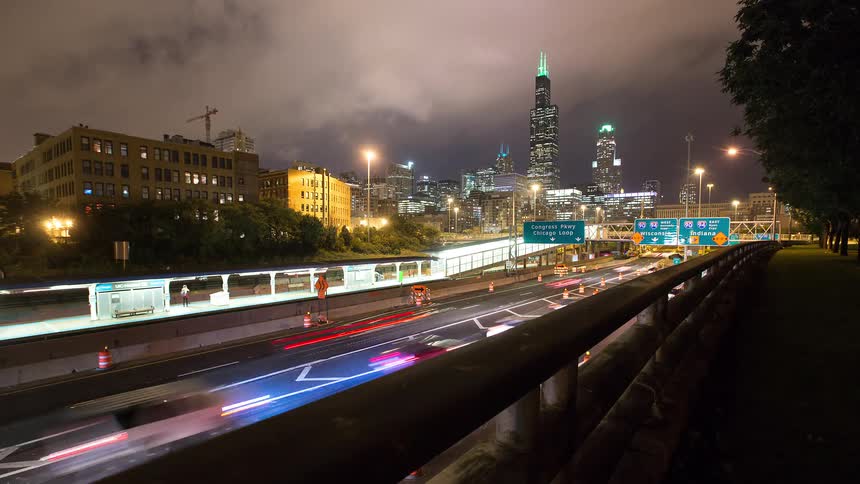 A sliding time-lapse reveals busy highway traffic and a train station with the iconic Chicago skyline illuminated at night