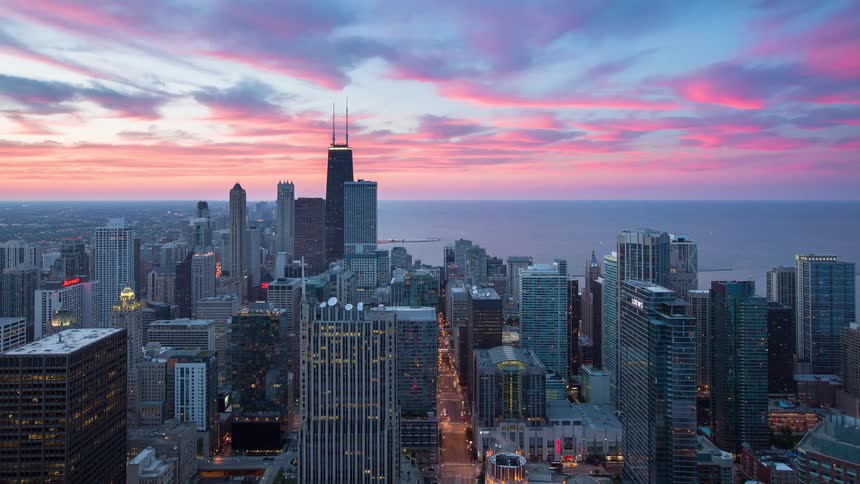 A stunning timelapse captures a vibrant pink sunset over the Chicago skyline as city lights begin to twinkle and traffic flows below