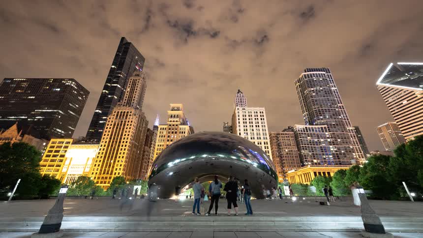 An energetic night timelapse captures the bustling activity around Chicago's iconic Cloud Gate sculpture, reflecting the magnificent city skyline