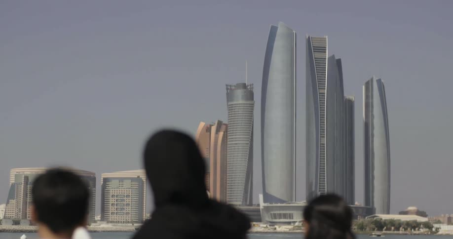 Woman and children look at tall skyscrapers across a body of water