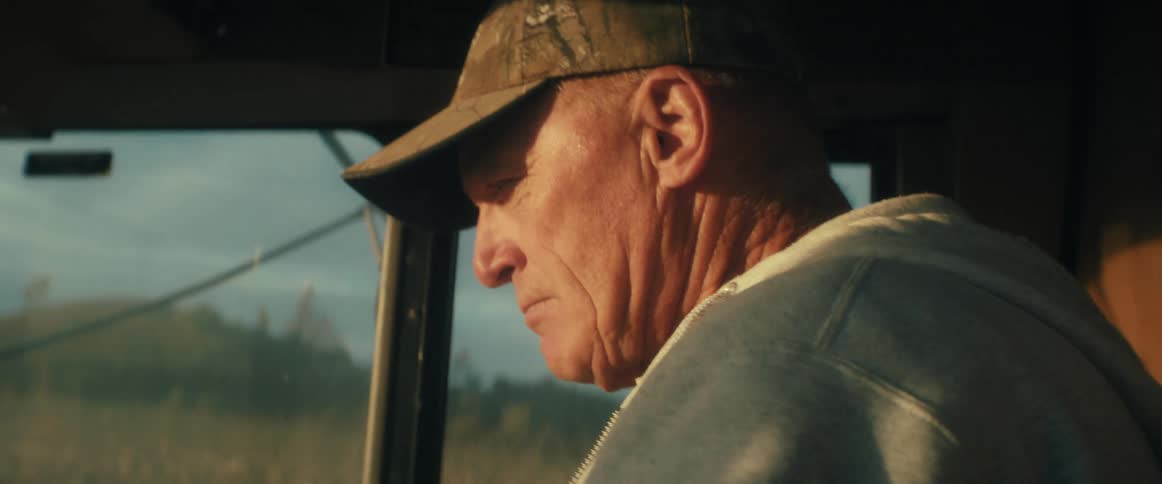 Slow motion close-up of a weathered farmer driving his combine through a golden cornfield during harvest