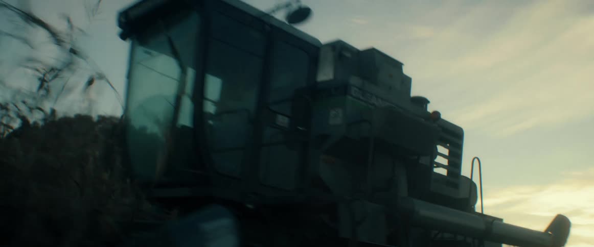 A combine harvester works its way through a rural cornfield at sunset, cutting down the crops