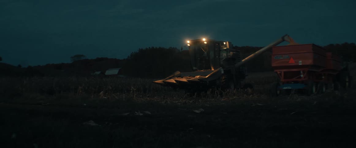 A combine harvester unloads its crop into a grain wagon during the twilight hours on a farm